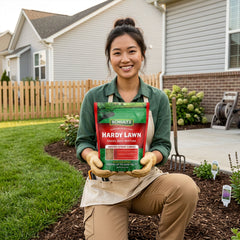 Woman holding a package of Schultz Hardy Lawn seed mix in front of a house with a garden.